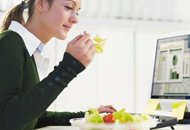 Frau isst Salat vor dem Computer