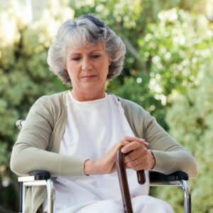 Sad-elderly-woman-sits-on-chair-and-holds-in-hands-stick