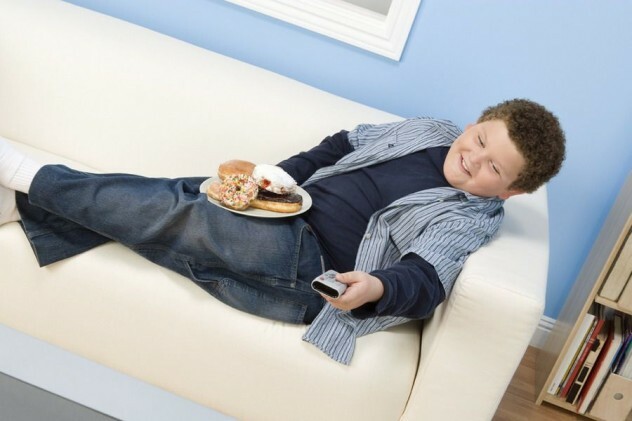 Junge sitzt auf der Couch mit Fernbedienung und Süßigkeiten